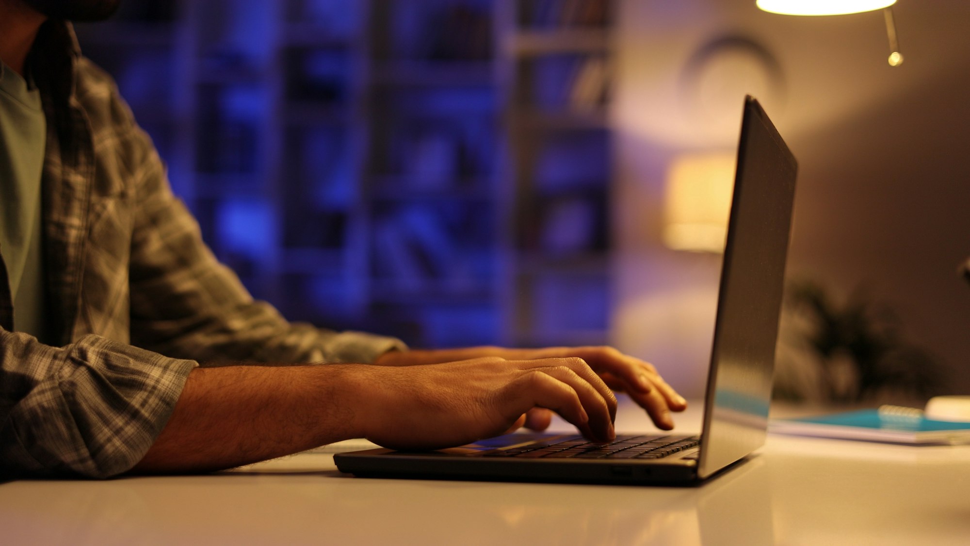 A young Arab student works on his laptop in the evening in the living room. A man with a beard works